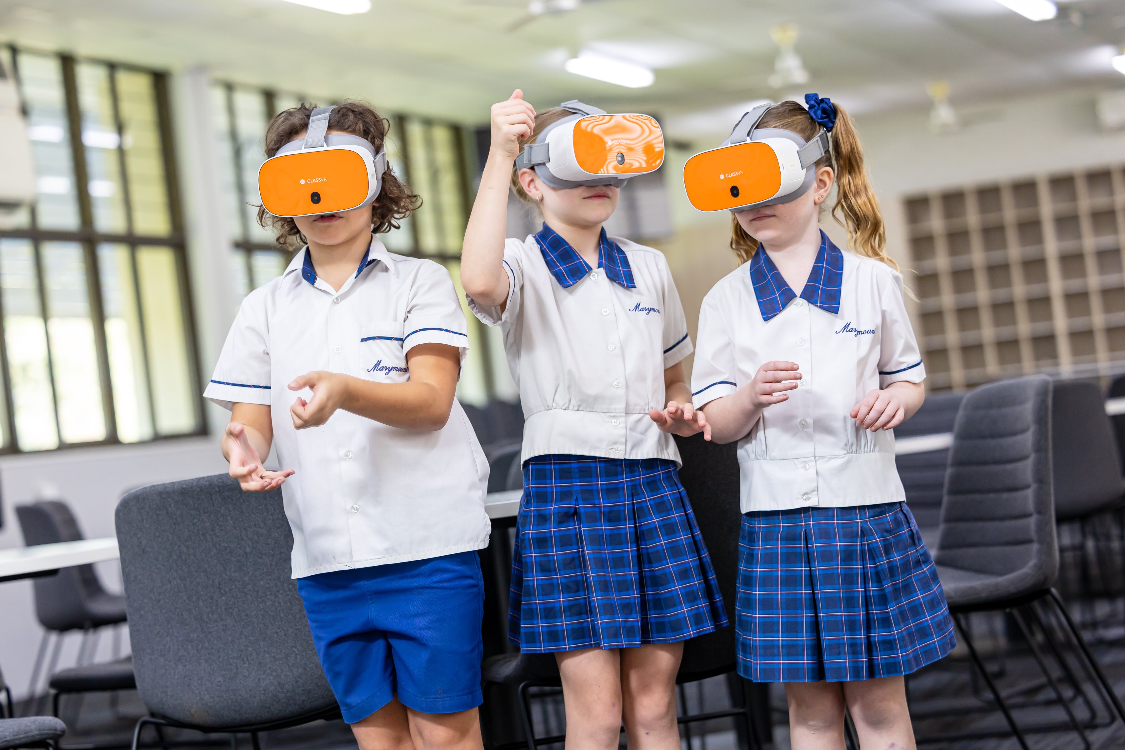 Three students in school uniforms wearing virtual reality headsets and interacting with a simulated activity in a classroom setting.